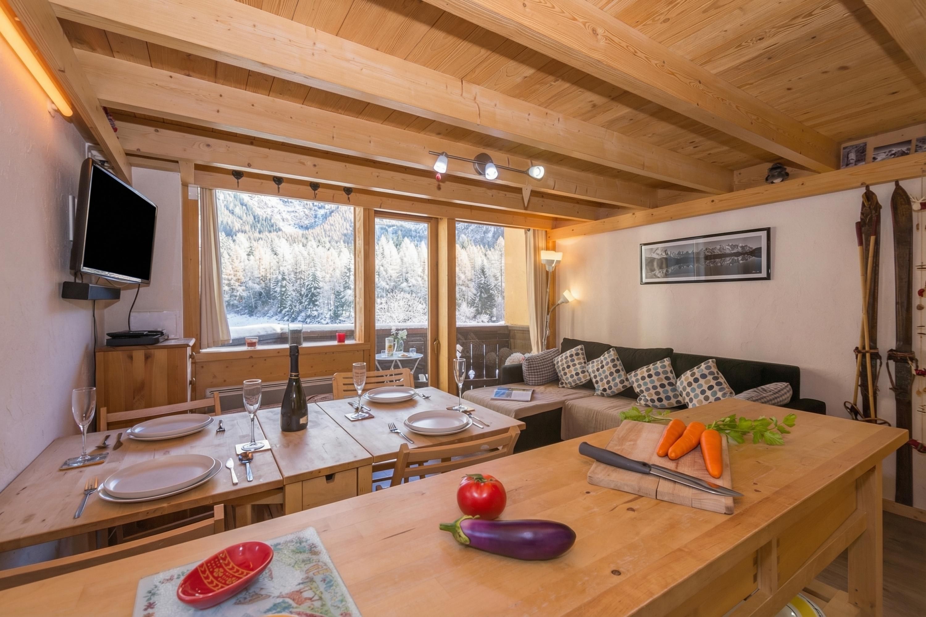Un intérieur en bois comprenant une table à manger pour deux personnes, un canapé et un téléviseur fixé au mur.