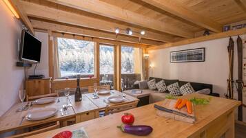 Un intérieur en bois comprenant une table à manger pour deux personnes, un canapé et un téléviseur fixé au mur.
