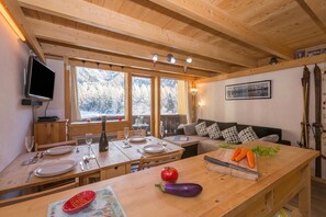 A wooden interior with a dining table set for two, a sofa, and a television mounted on the wall. - Grand Roc B220 260m from Slopes, View, Parking & WiFi, Argentière (Chamonix), France (Argentière (Chamonix))