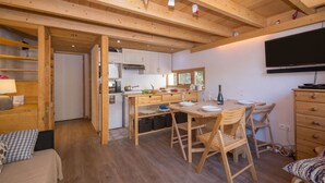 A cozy room with a wooden ceiling, a dining table with chairs, a TV mounted on the wall, and a bed with a patterned pillow. - Grand Roc B220 260m from Slopes, View, Parking & WiFi, Argentière (Chamonix), France (Argentière (Chamonix))
