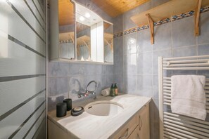 Een badkamer met een wastafel, spiegel, handdoekhouder en een raam met jaloezieën.