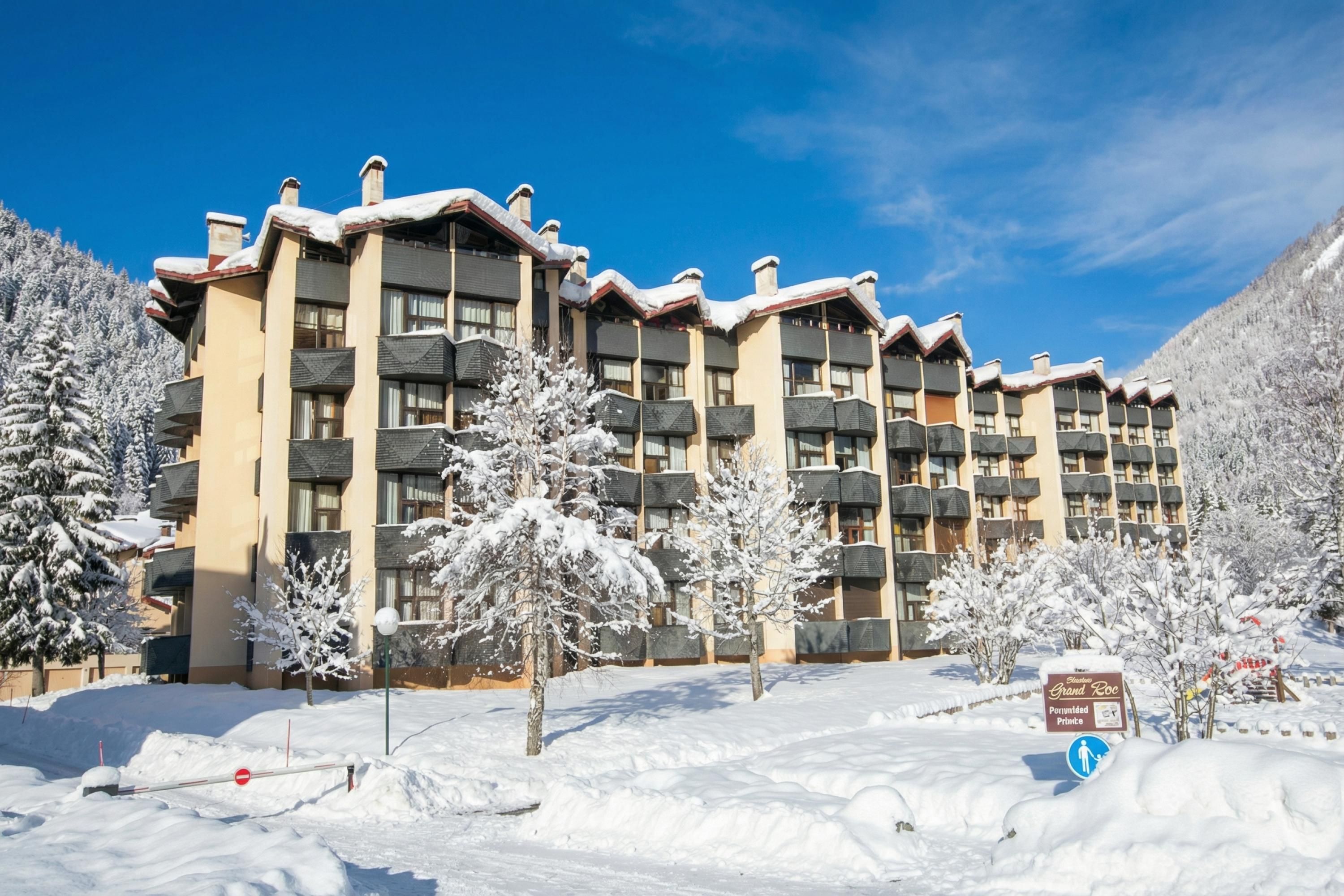 Un hôtel à plusieurs étages doté de balcons, entouré d’arbres couverts de neige et surplombant un ciel dégagé.