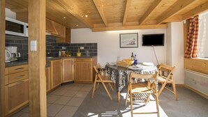 A kitchen with wooden cabinets, a tiled backsplash, a dining table with chairs, and a television mounted on the wall.
