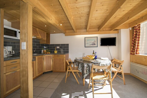 Une cuisine avec des meubles en bois, un pare-feu en carreaux, une table à manger avec des chaises et un téléviseur fixé au mur.
