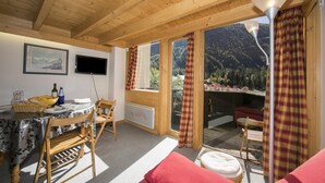 A wooden interior with a dining area, a sofa, and a view of a mountainous landscape.