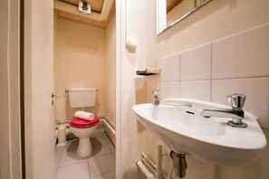 Une salle de bain avec un lavabo blanc, des toilettes avec un abattant rouge et un miroir au-dessus du lavabo.