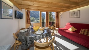 A dining area with a table set for two, wooden chairs, a red sofa, and a television on the wall.