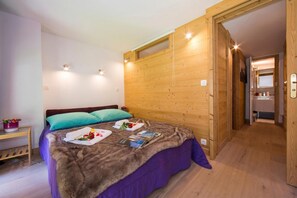 Una camera da letto con una parete in legno, un letto con copriletto viola e un tavolino con un contenitore rosa.