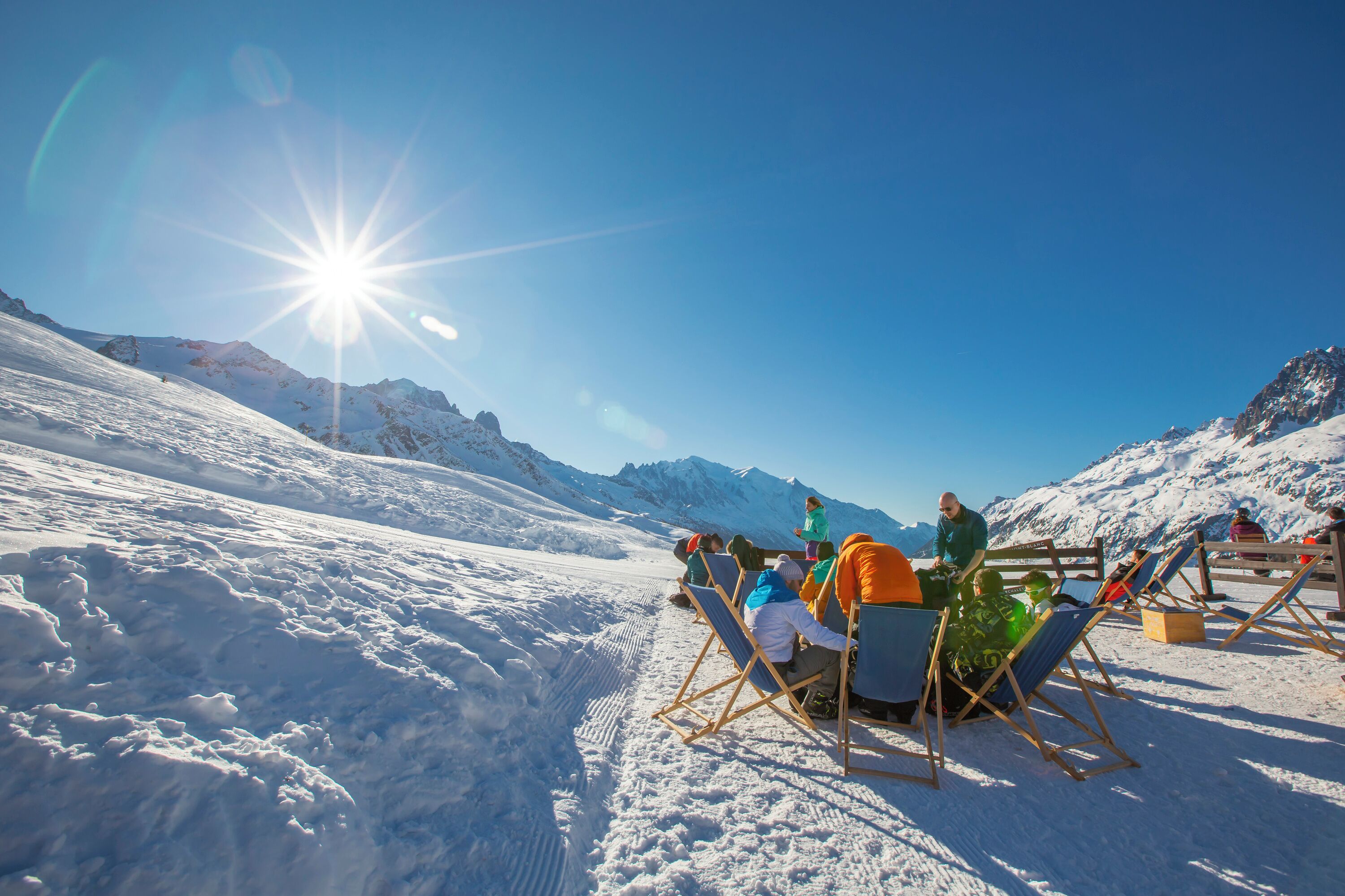 A group of people seated on outdoor chairs in a snowy landscape with mountains in the background.