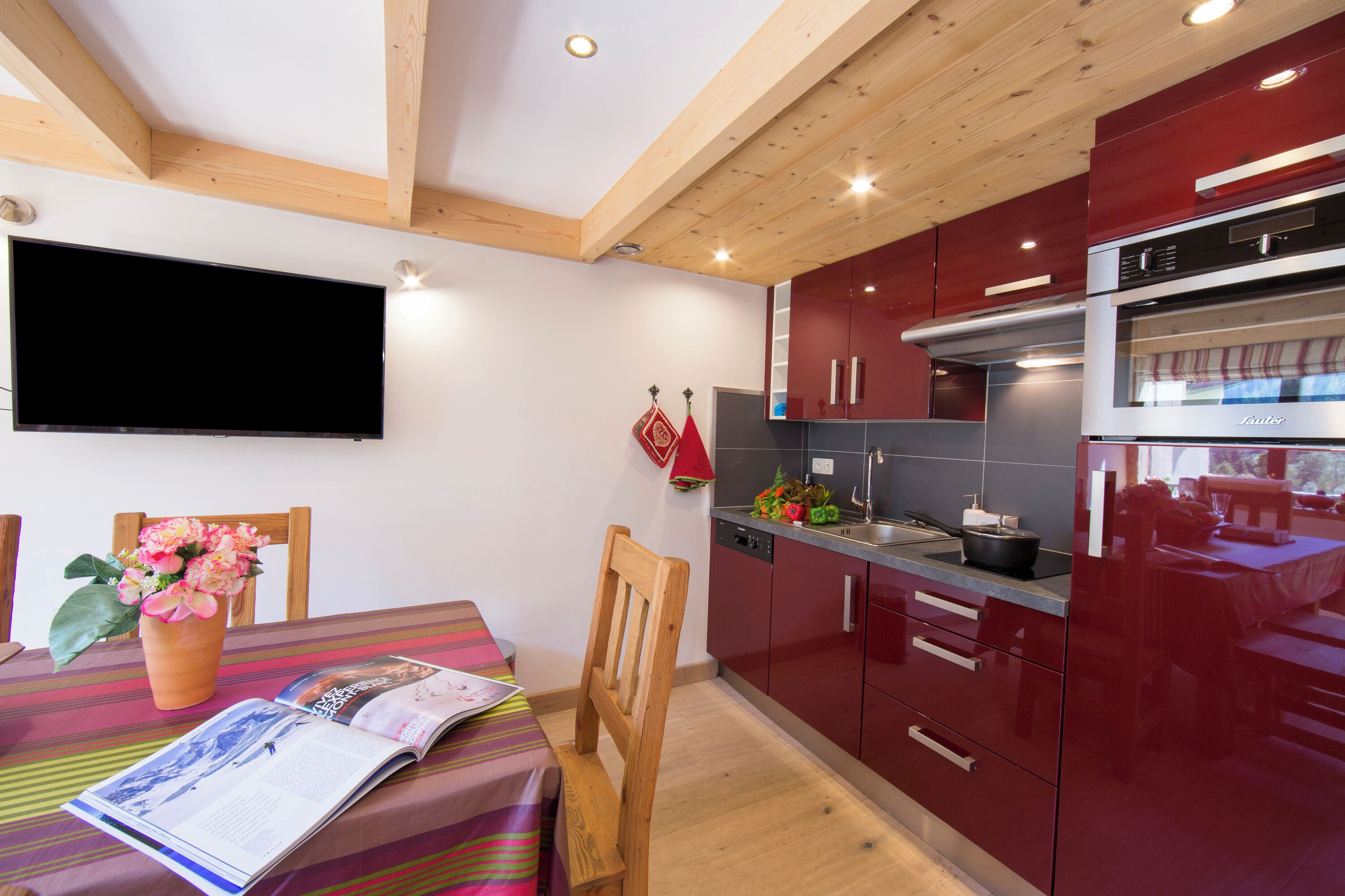 Eine moderne Küche mit roten Schränken, einem eingebauten Backofen und einem Essbereich mit Tisch und Stühlen.
