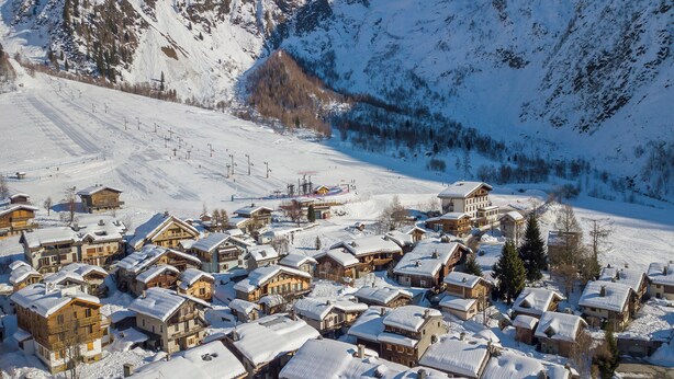 A snow-covered village with traditional wooden houses, a ski lift, and a mountain backdrop.