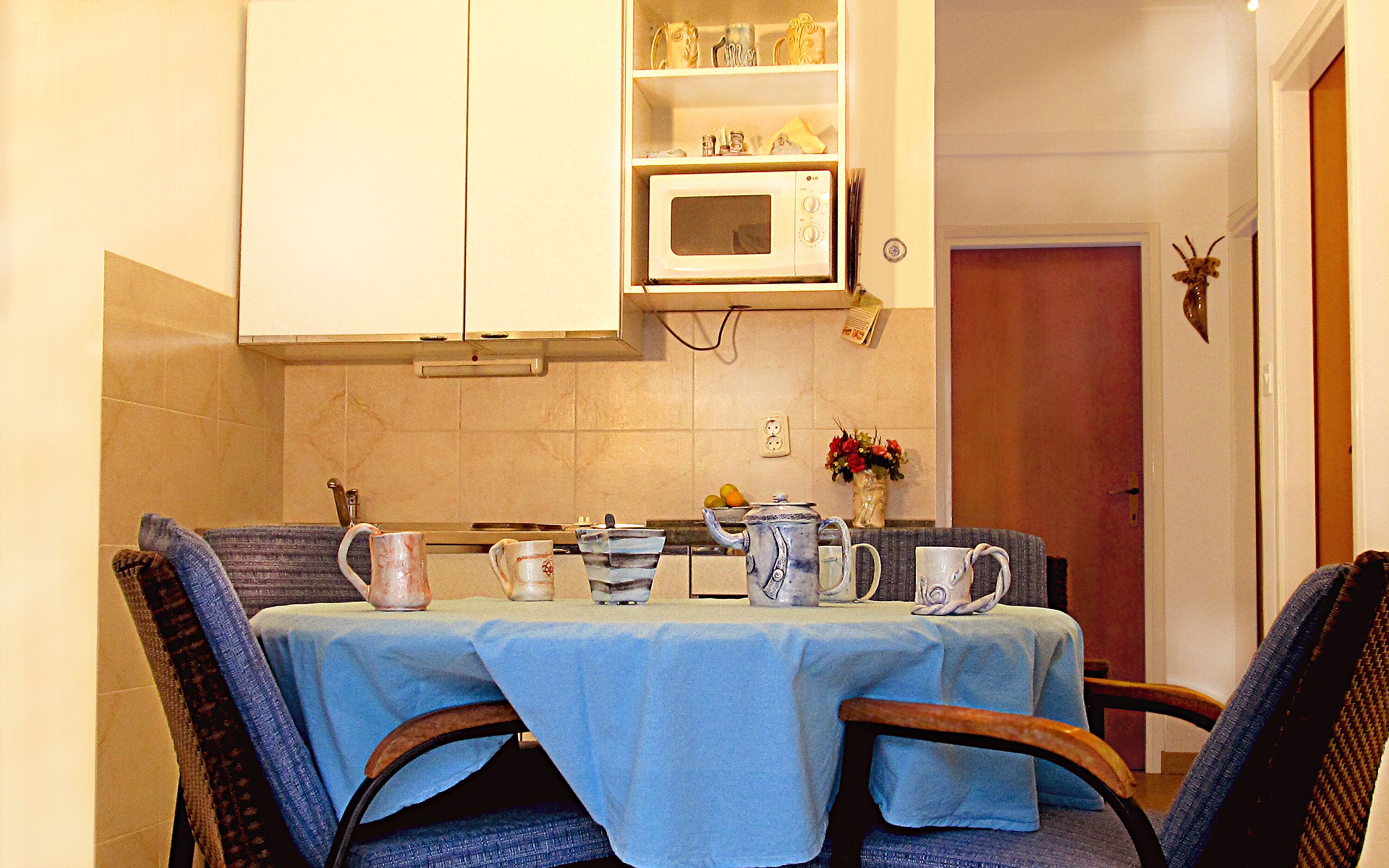 Un comedor con una mesa dispuesta para dos personas, un microondas encima de la mesa y un armario sobre el microondas.
