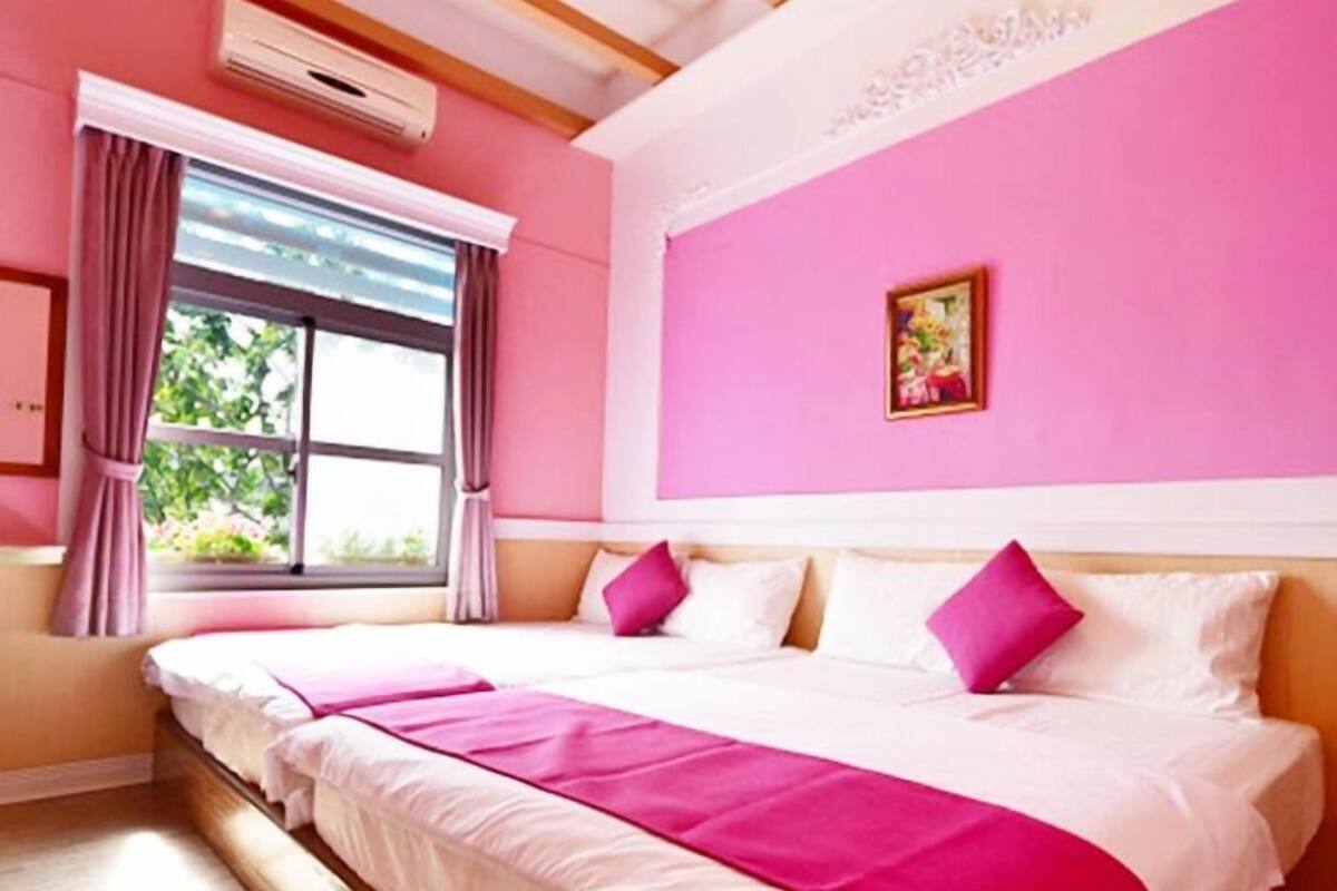 Quarto de hotel com uma cama grande, paredes cor-de-rosa e uma janela com cortinas.
