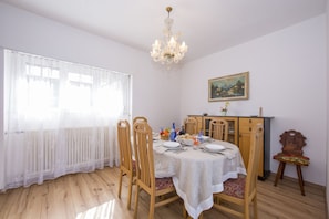 Una sala da pranzo con un tavolo imbandito per quattro persone, sedie in legno, un lampadario, un termosifone e un quadro appeso al muro.