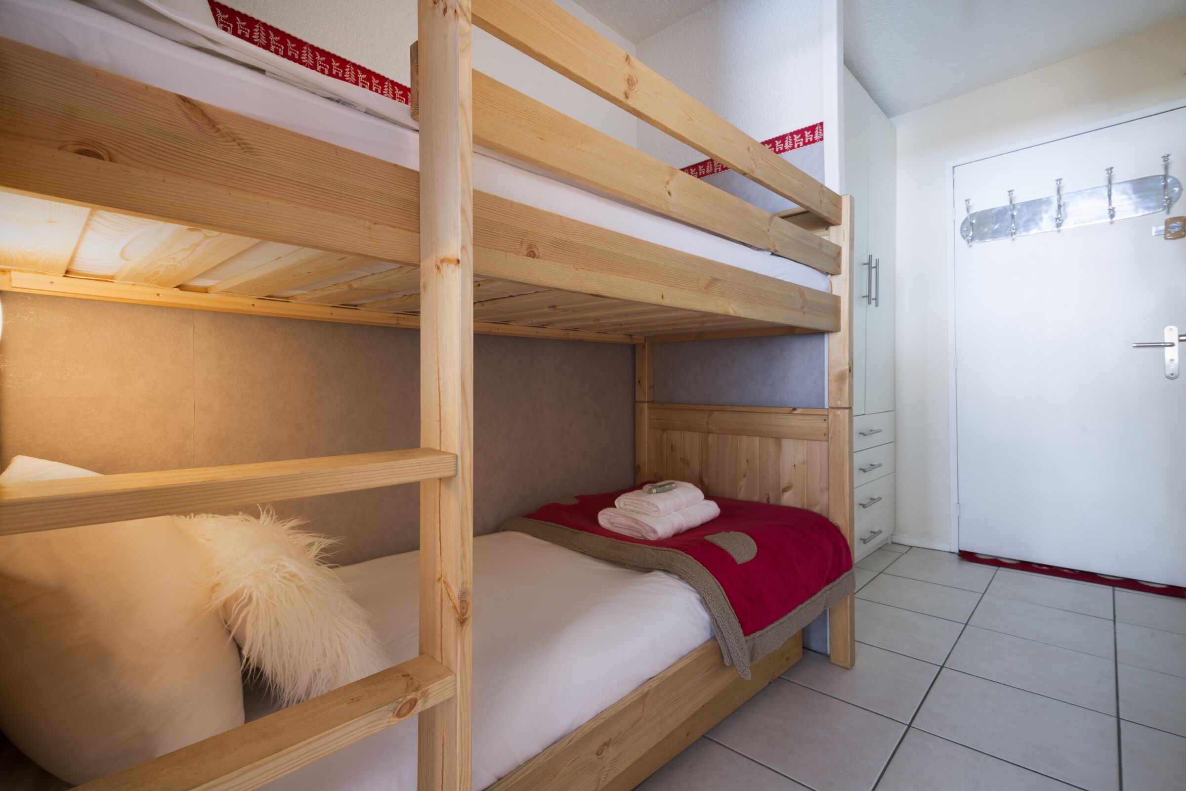 A bunk bed room with a wooden frame, a white pillow, and a red blanket.
