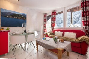 A cozy room with a dining table, chairs, a red sofa, and a window with a view of a snowy landscape.