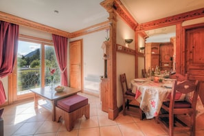 A dining area with a table, chairs, and a bench. There is a window with curtains and a view of greenery. - Résidence Le Cristal - Nant Blanc 4, Argentière (Chamonix), France (Argentière (Chamonix))