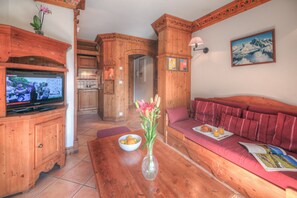 Un intérieur en bois avec une télévision, un vase de fleurs, un saladier de fruits et un canapé avec un magazine.