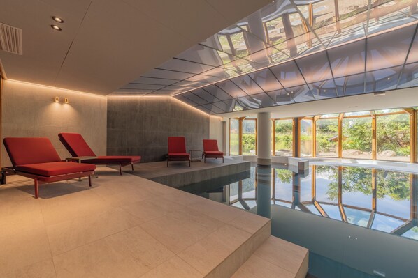 Piscina interior moderna com cadeiras de descanso vermelhas e teto de vidro.