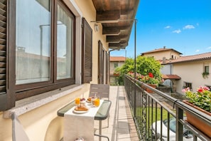 A balcony with a table set for breakfast, a railing, and a view of the neighborhood.