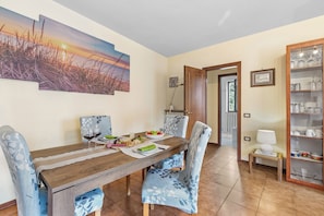 A dining area with a wooden table, chairs, a painting, a cabinet with glassware, and a door leading to another room.