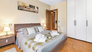 A neatly made bed with towels, a painting on the wall, and a wardrobe.