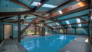 Una piscina interior con vigas de madera, suelo de baldosas y techo transparente.