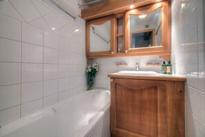 Un baño con tocador de madera, azulejos blancos, una bañera y un espejo sobre el tocador.