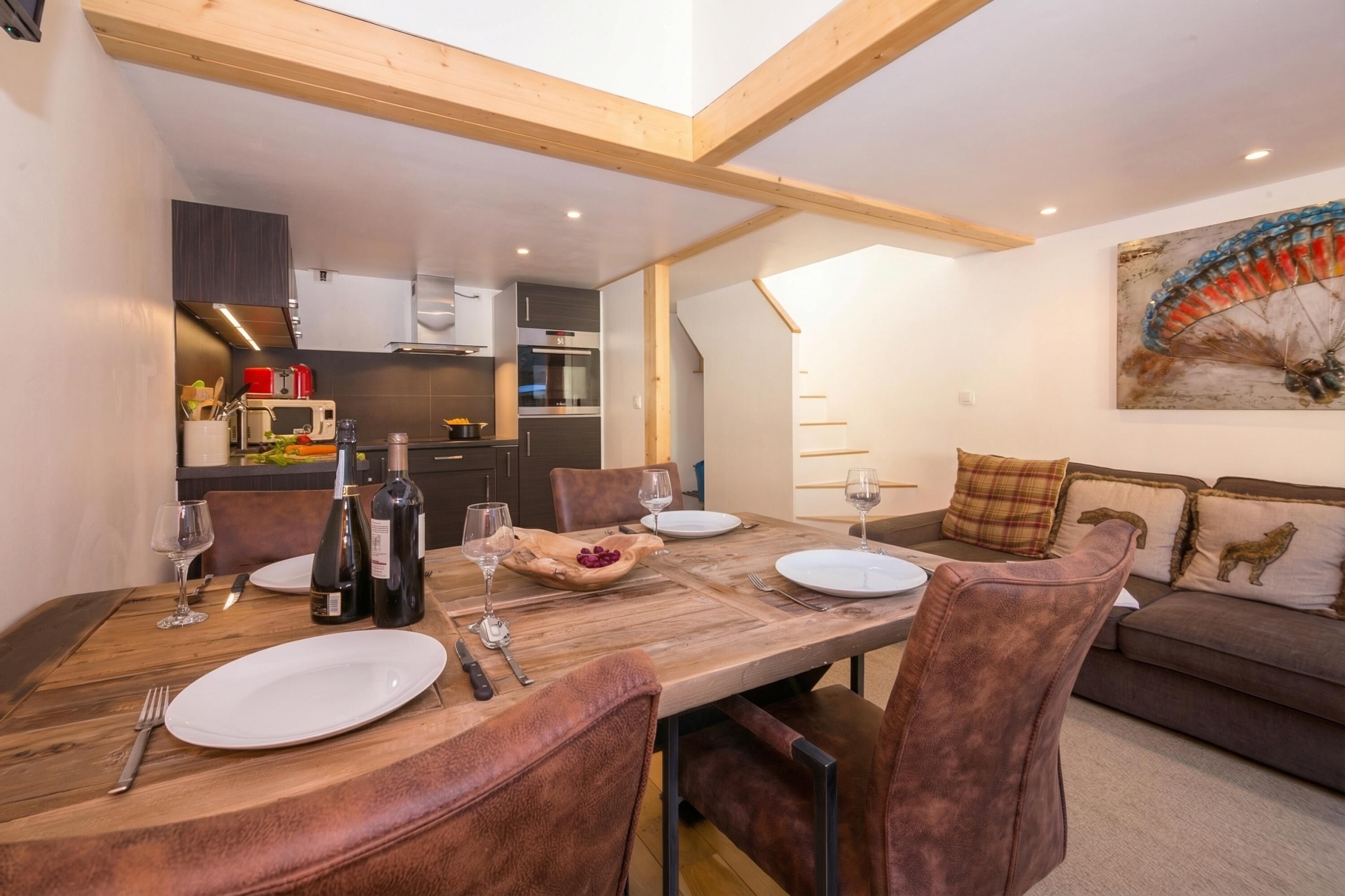 Un coin repas avec une table en bois, des chaises en cuir et une cuisine en arrière-plan.