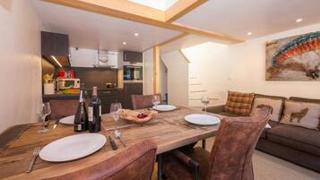Un coin repas avec une table en bois, des chaises en cuir et une cuisine en arrière-plan.