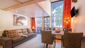 A modern living room with a sofa, dining table, chairs, a TV, and a large window with curtains. - Grand Roc B22 260m from Slopes, View, Parking & WiFi, Argentière (Chamonix), France (Argentière (Chamonix))
