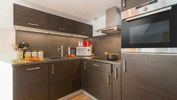 Une cuisine moderne avec des meubles de couleur sombre, un four en acier inoxydable et un four à micro-ondes.