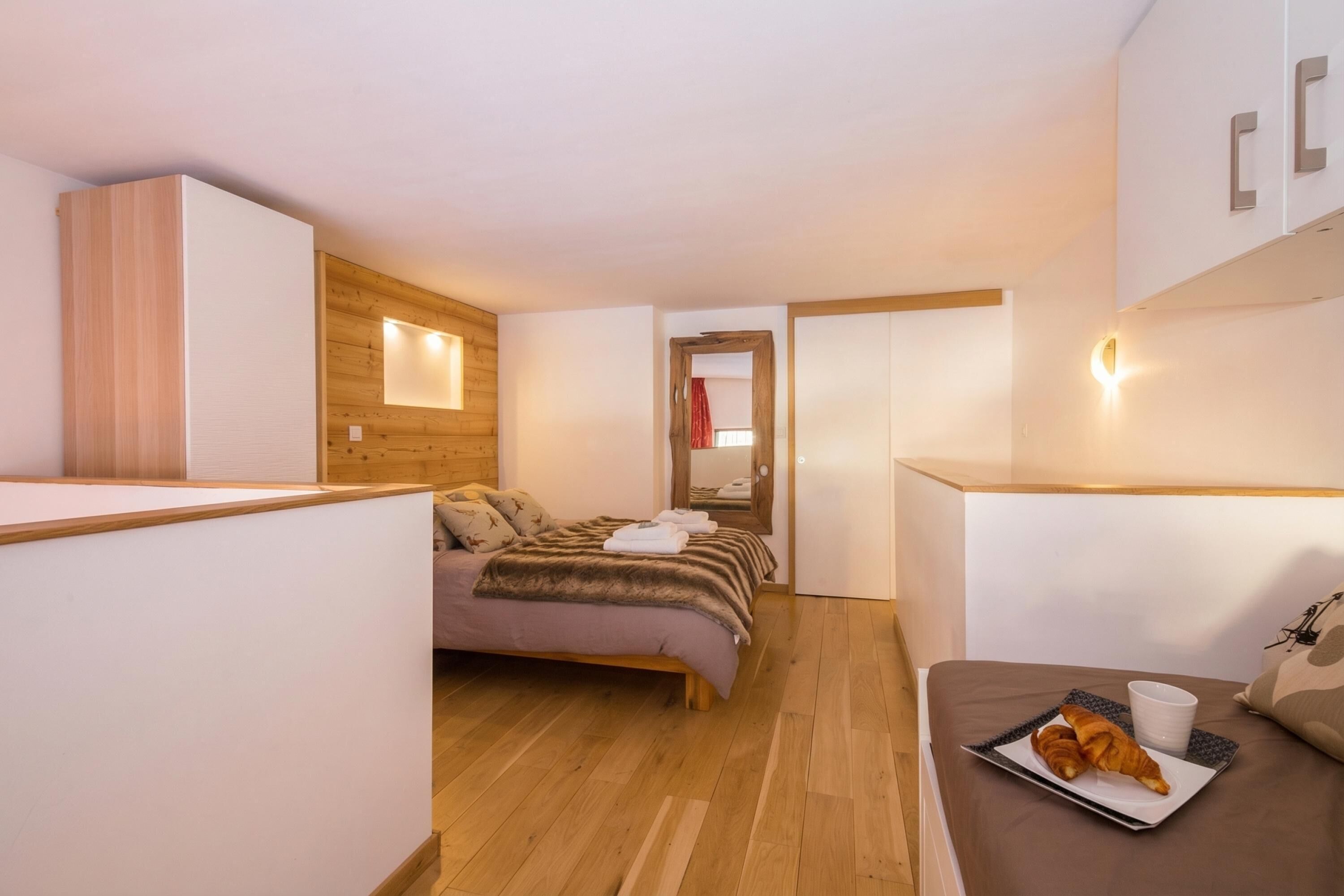 Een moderne hotelkamer met een bed, een klein tafeltje met croissants, een kopje en een houten wandpaneel.