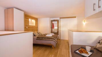 Een moderne hotelkamer met een bed, een klein tafeltje met croissants, een kopje en een houten wandpaneel.