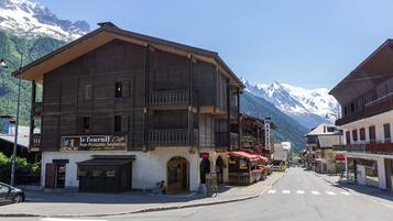 Un bâtiment en bois avec une enseigne indiquant la présence d’un café, une rue avec des passages piétons et, au loin, des montagnes enneigées.