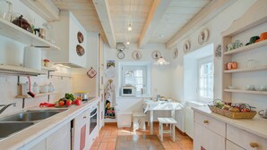 A kitchen with white cabinets, a sink, and a stove. There are shelves with dishes and a window with curtains. - Antico Chalet, Livigno, Italy (Livigno)