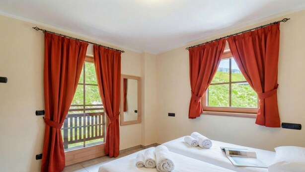 Ein Hotelzimmer mit zwei Betten, roten Vorhängen, einem Fenster mit Blick und einem Nachttisch mit Buch und Handtüchern.