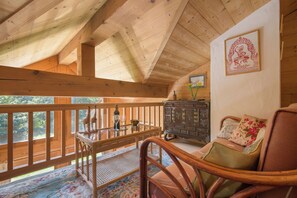 Interior de uma cabana de madeira com varanda, mesa de jantar, cadeira de vime e um objeto decorativo na parede.