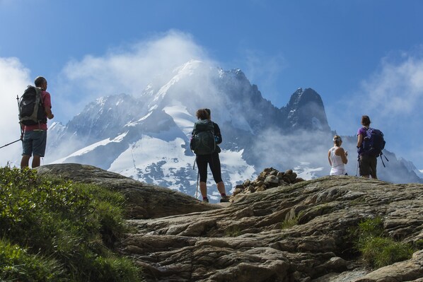 Um grupo de pessoas em um pico rochoso, com montanhas cobertas de neve ao fundo.