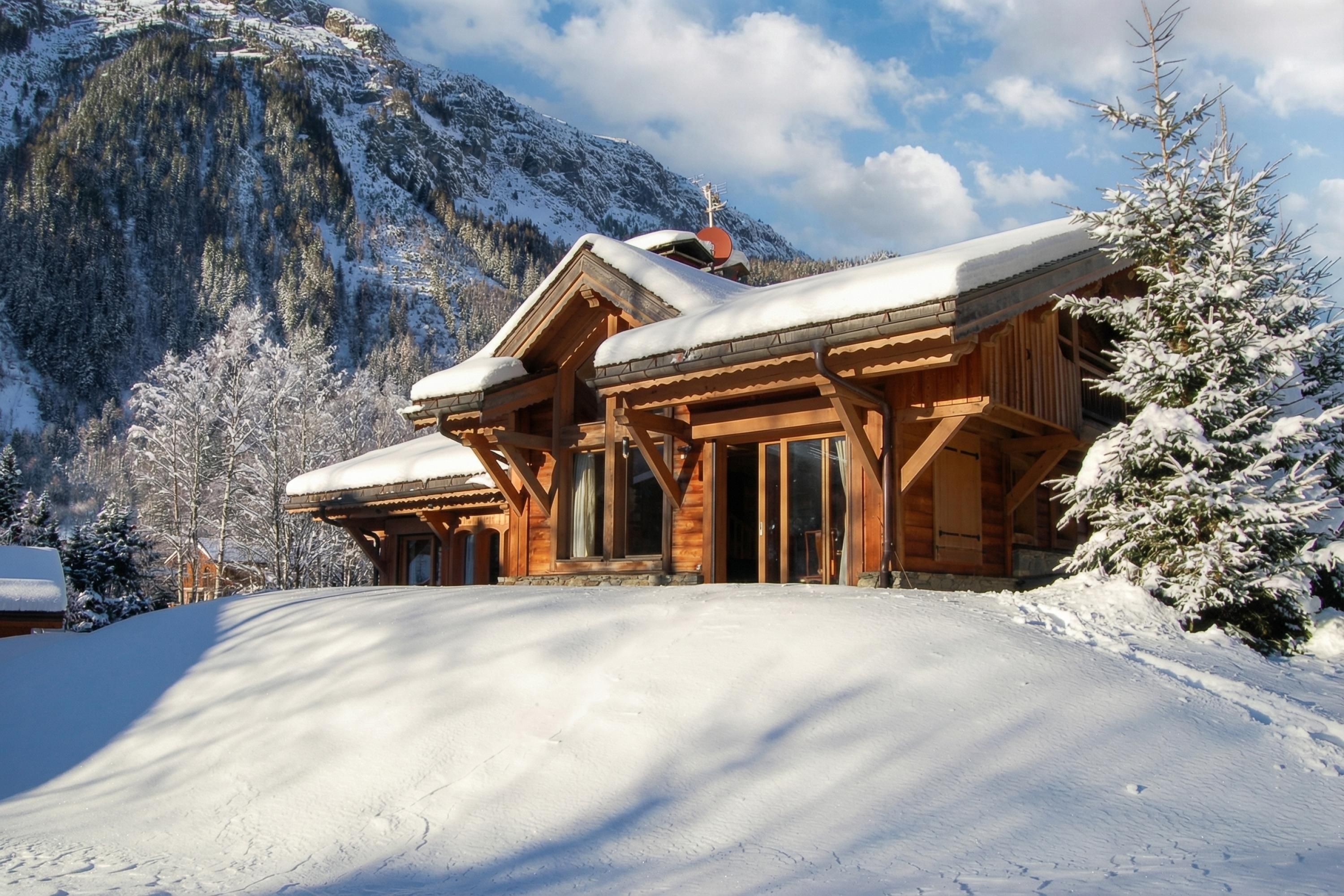 A wooden chalet with a snow-covered roof, set against a mountainous backdrop.