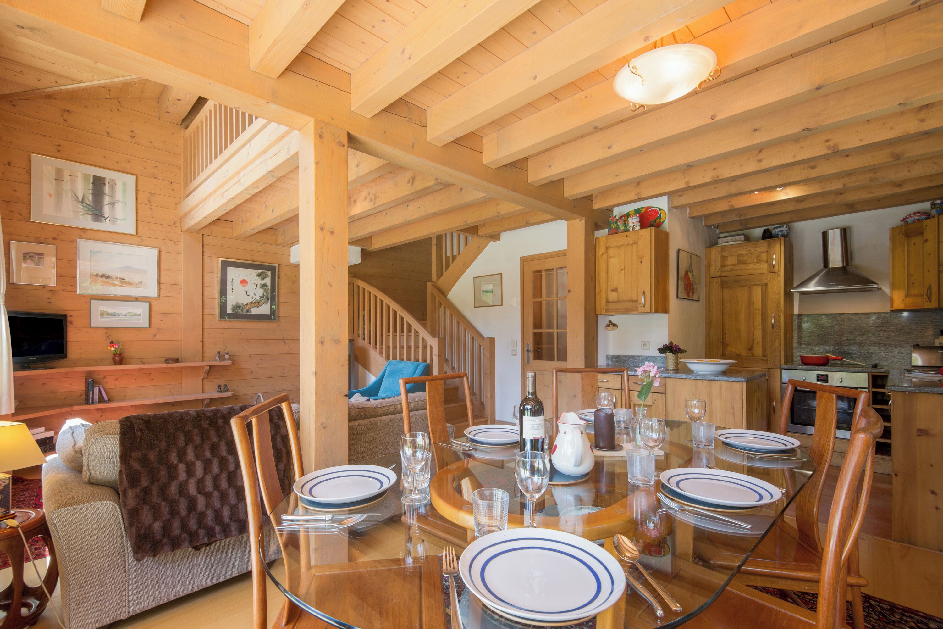 Un interior de madera con una mesa de comedor preparada para cuatro personas, armarios de madera y una escalera que sube a otro nivel.