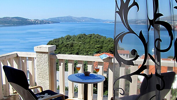A balcony with a chair and a table, overlooking a scenic view of the sea and hills. - Sea view Apartment in Trogir near the beach (Trogir)