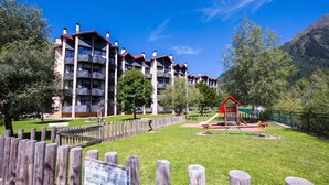 Un hôtel à plusieurs étages doté de balcons, d’une aire de jeux et d’une cour clôturée.