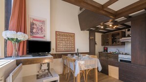 Un coin repas avec une table dressée pour quatre personnes, des chaises en bois, un téléviseur posé sur un meuble et une affiche accrochée au mur.