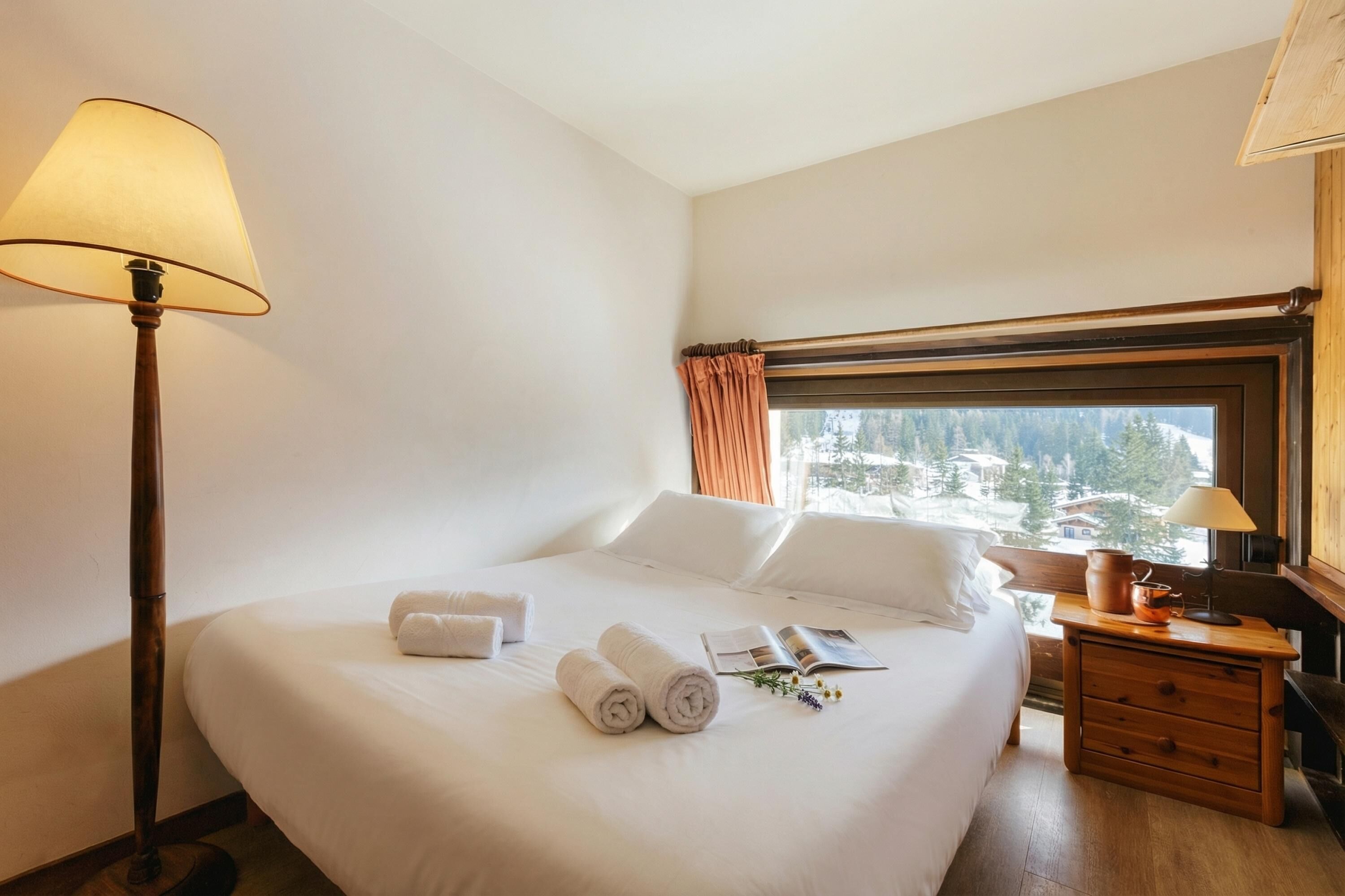 Een hotelkamer met een bed, een lamp, een nachtkastje en een raam met uitzicht.