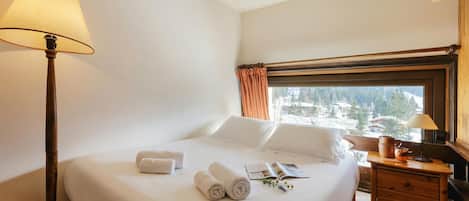 Une chambre d’hôtel avec un lit, une lampe, une table de chevet et une fenêtre donnant sur un beau paysage.