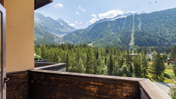 Un balcon donnant sur un paysage montagneux, avec une balustrade en bois et une porte.