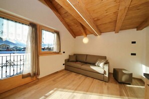 A room with a wooden ceiling, a sofa, a small table, and a window with a view of a mountain.