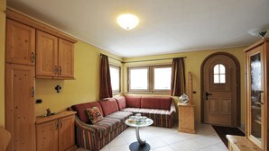 A cozy living room with a sectional sofa, a small round table, wooden cabinets, and a door with a frosted glass panel.