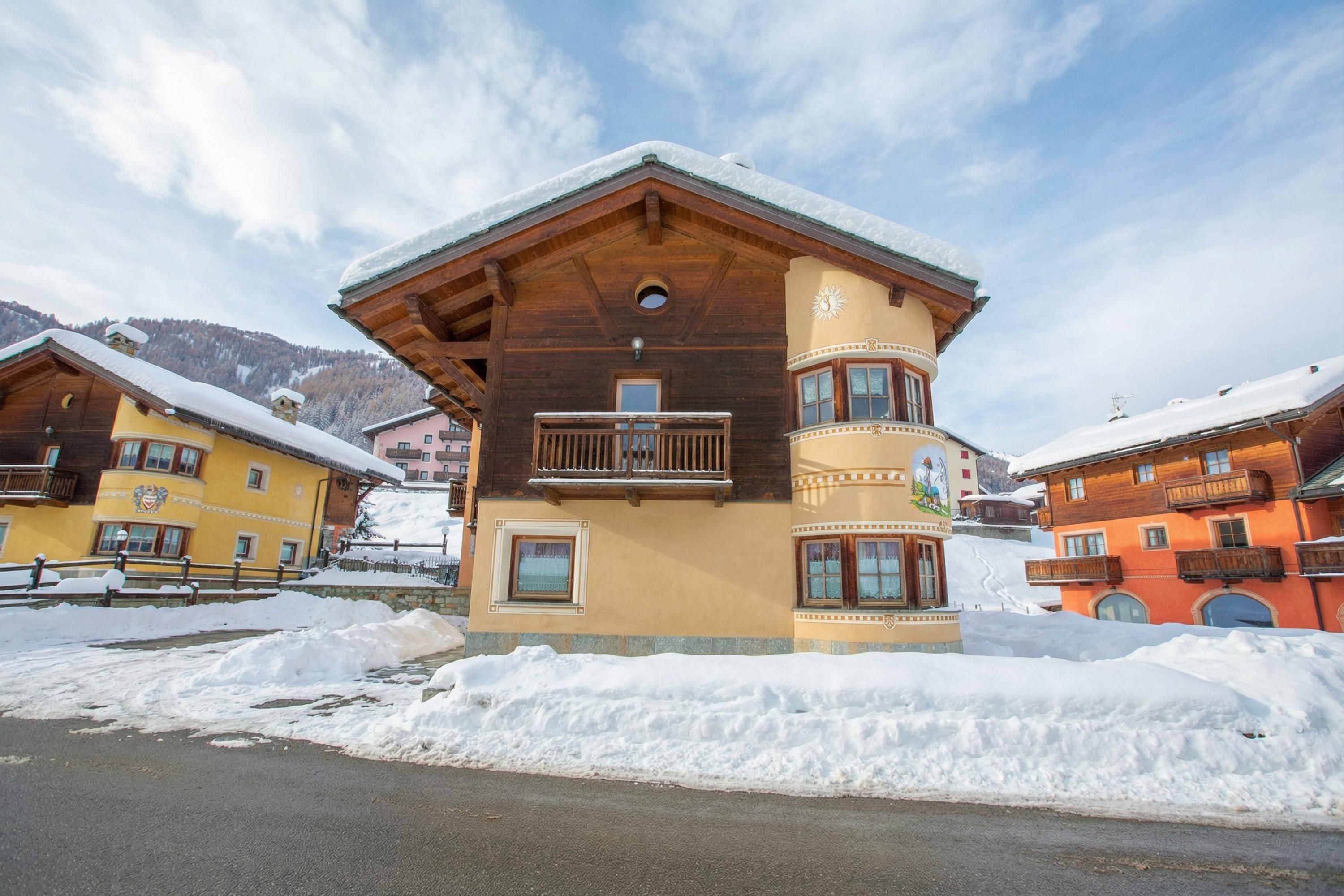 A multi-story wooden building with balconies, a snow-covered roof, and a mountainous backdrop.